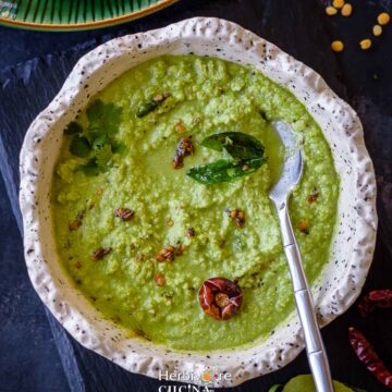 Coconut cilantro chutney in a white bowl with tempering on top and a spoon on the side.