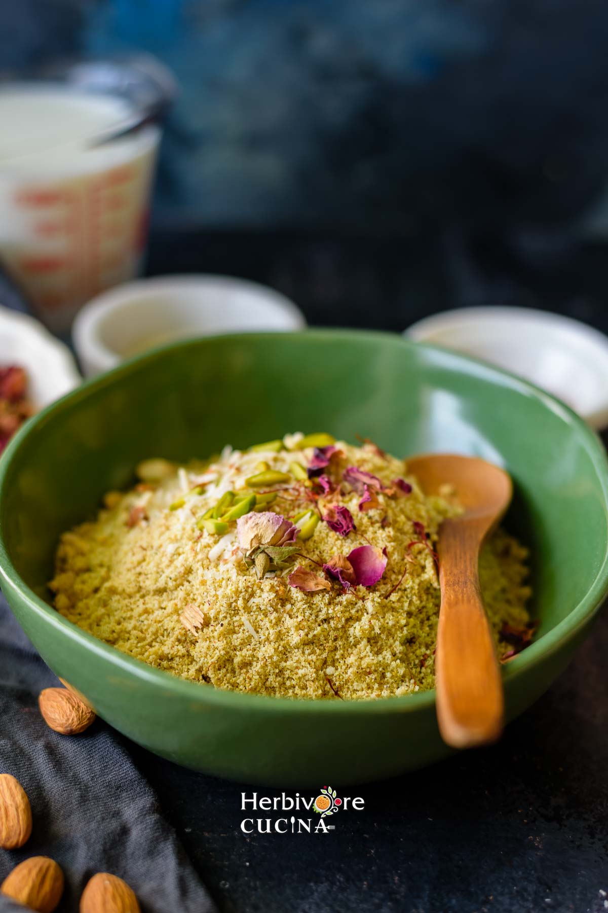 Milk masala powder in a green bowl with saffron and rose petals on it and a spoon in it. 