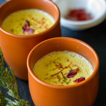 Masala Milk in earthern glasses with some saffron strands in a small bowl behind it.