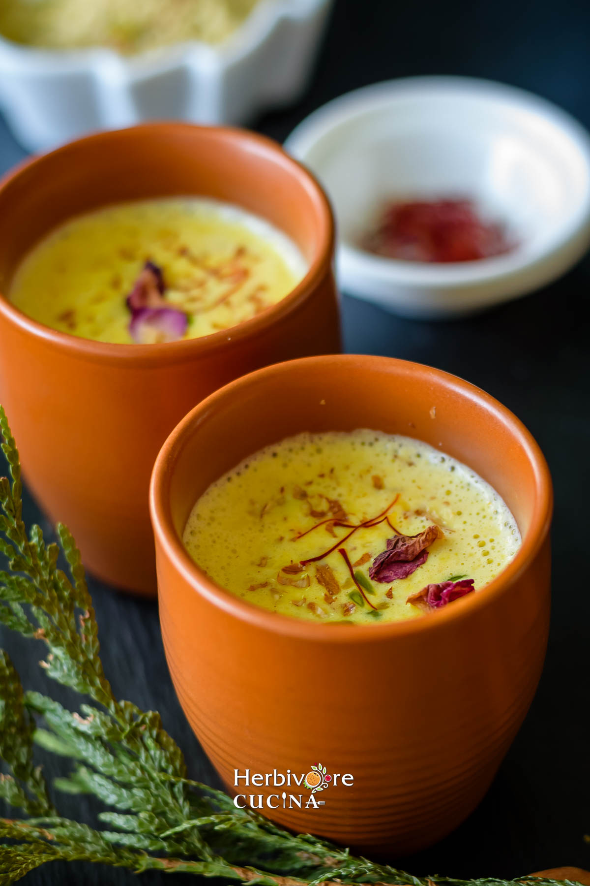 Masala Milk in earthern glasses with some saffron strands in a small bowl behind it. 