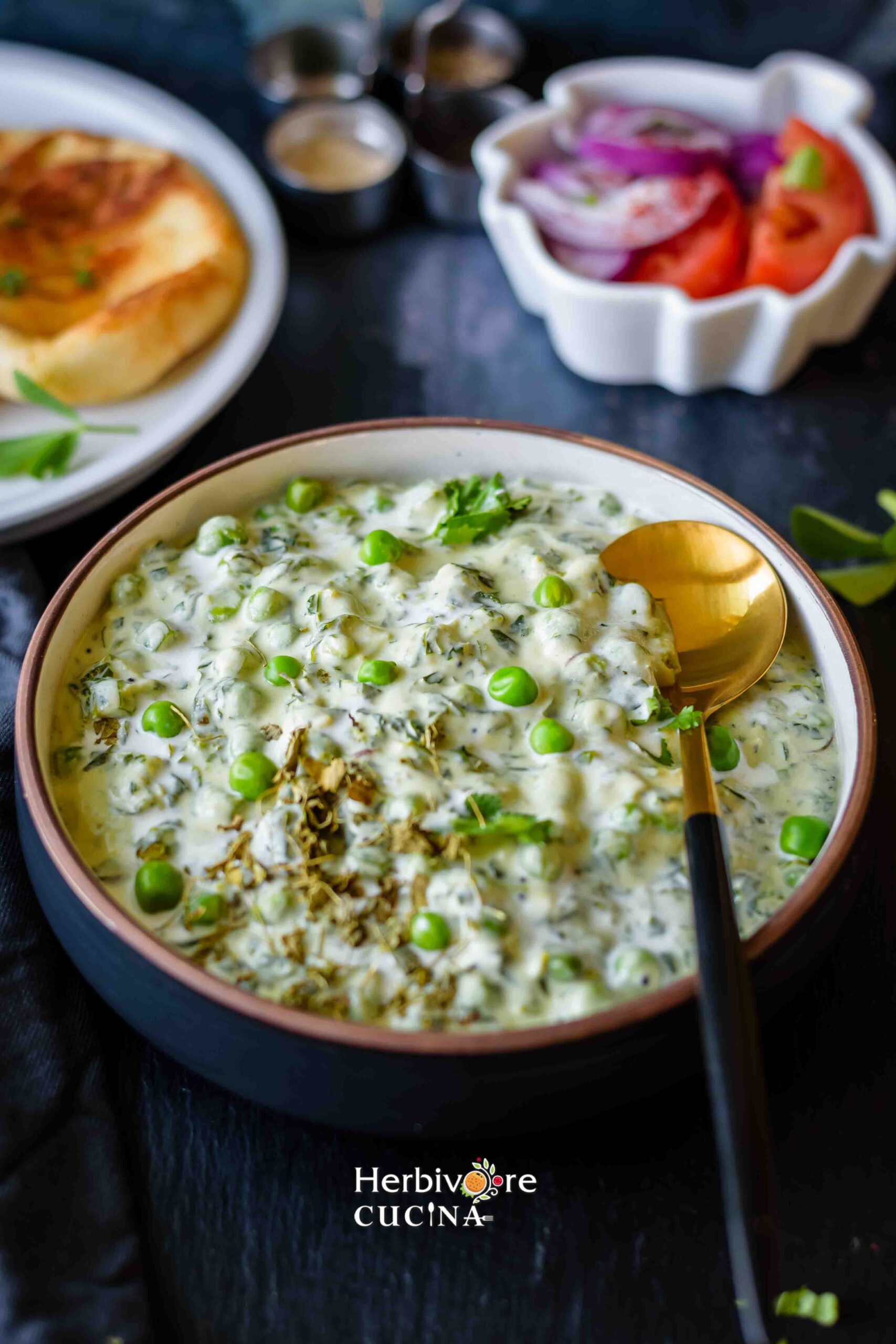 A bowl with methi mater malai in it with a spoon; and some salad and naan on the sides. 