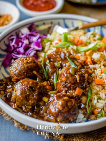 Vegetable Manchurian in gravy with fried rice and cabbage salad in a plate with some hot sauce on the side.