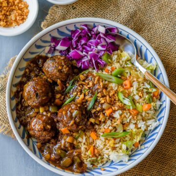 A plate with non-fried manchurian with fried rice and cabbage salad with sauce on the side.