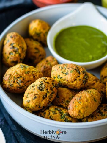 A large bowl filled with Non-Fried Methi Muthiya with a small bowl of cilantro chutney on the side.