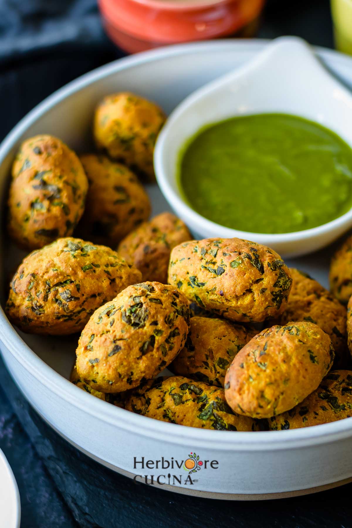 A large bowl filled with Non-Fried Methi Muthiya with a small bowl of cilantro chutney on the side. 