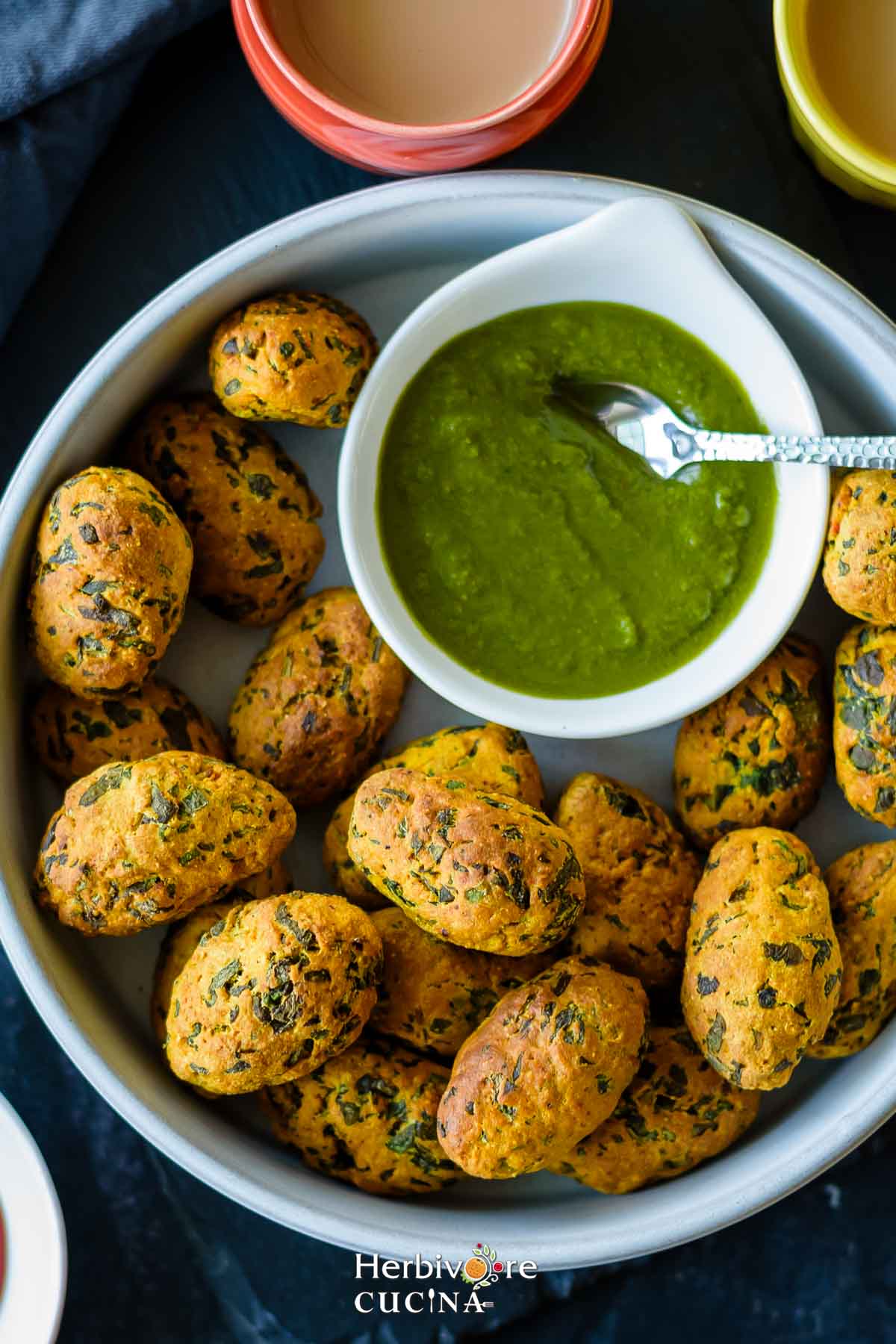 Air fryer methi muthiya in a white plate with a small bowl filled with spicy cilantro chutney and masala chai on the side. 