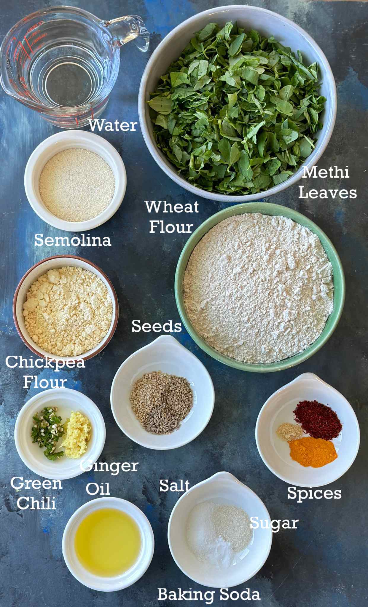 Ingredients for non-fried methi muthiya in small bowls on a dark surface with labels. 