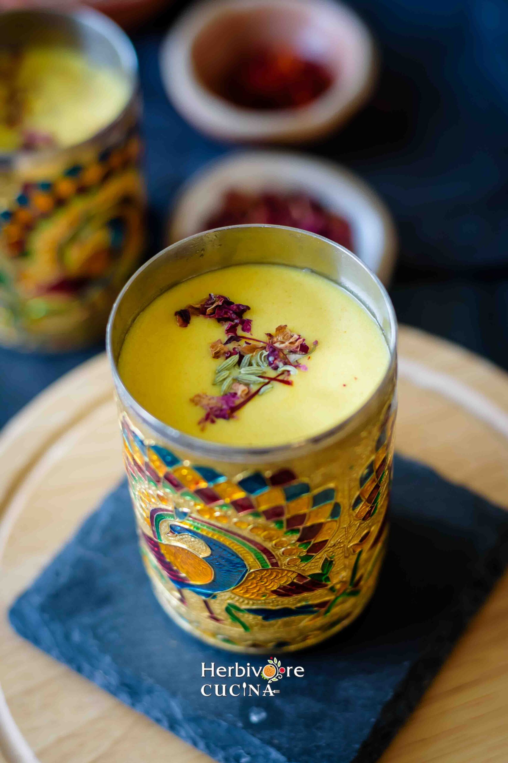 A glass of saffron thandai in an Indian glass, topped with fennel and rose petals. 