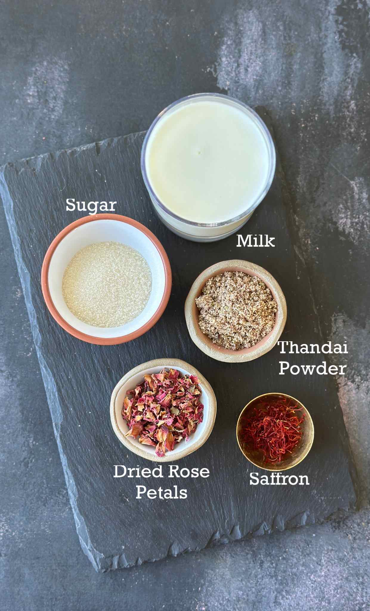 Ingredients to make Thandai in small bowls on a slate background. 
