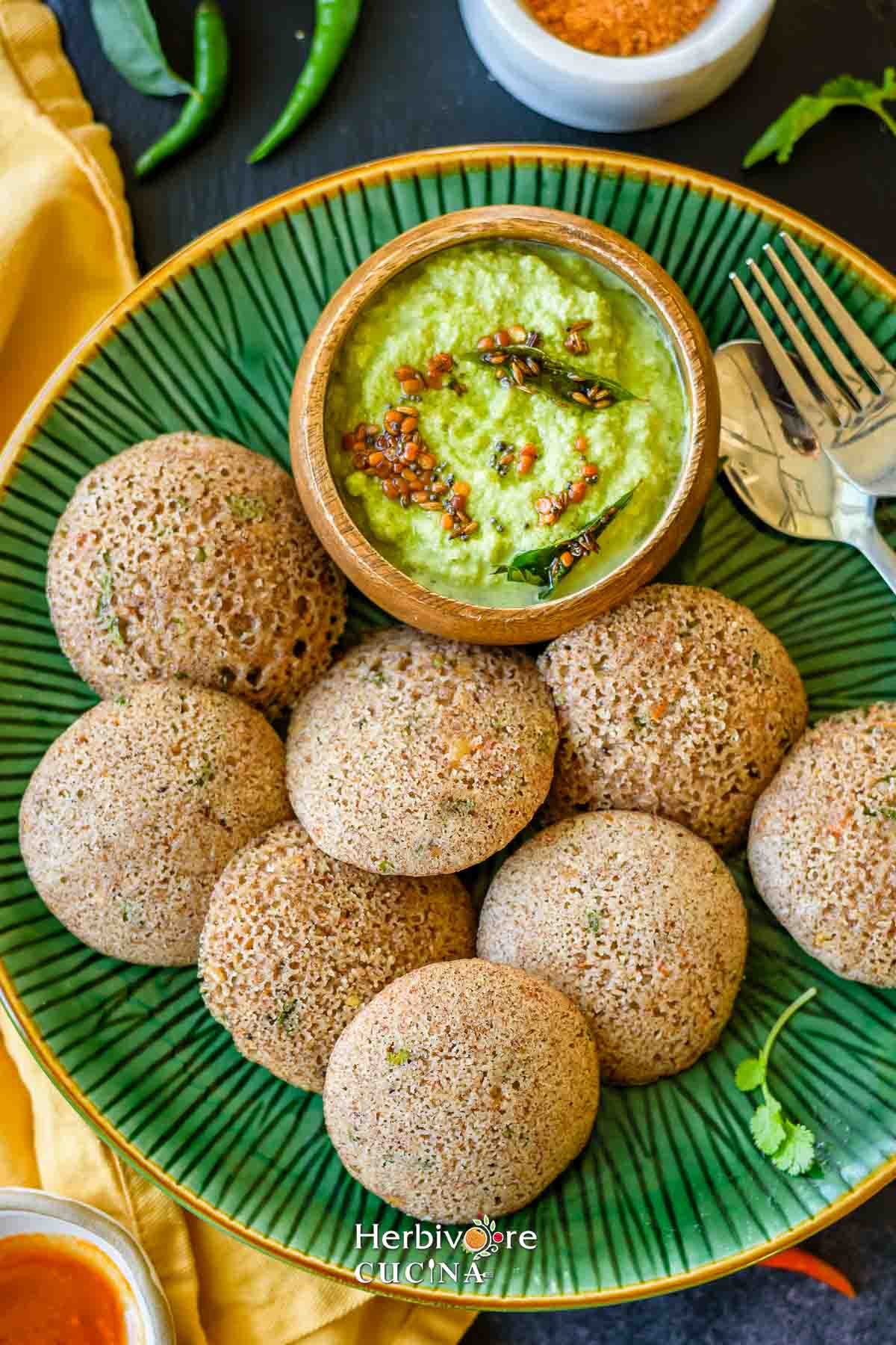 A green plate with ragi rava idli and cilantro coconut chutney on the side. 