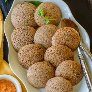 An oval platter with instant ragi idli; served with chutneys on the side.