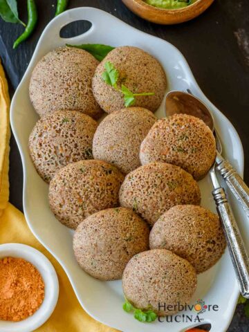 An oval platter with instant ragi idli; served with chutneys on the side.