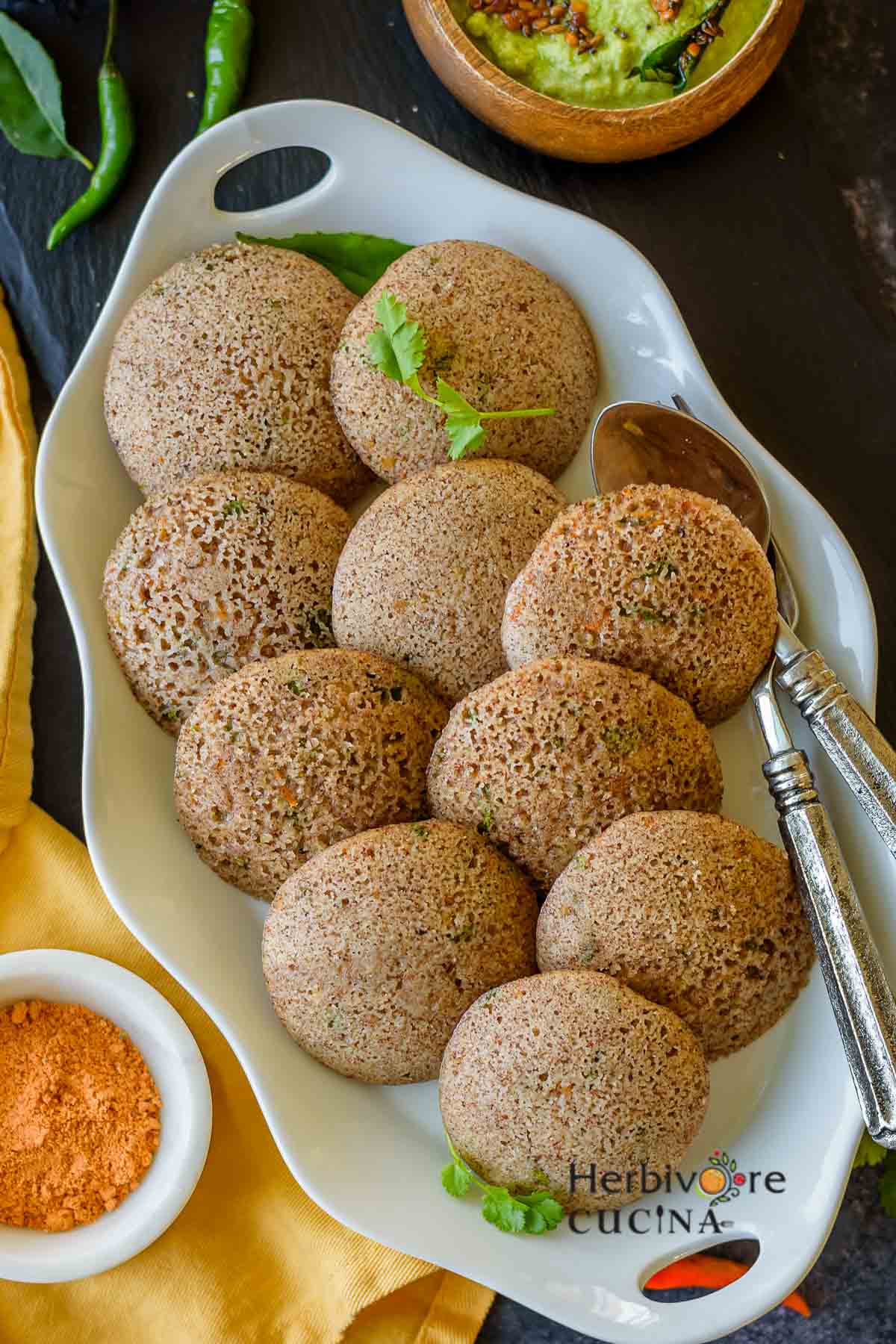 An oval platter with instant ragi idli; served with chutneys on the side. 