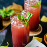 Two glasses filled with kokum sharbat topped with mint leaves and served with ice on a slate platter.
