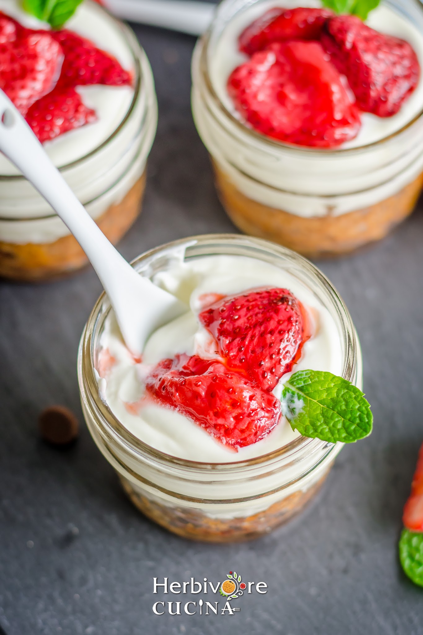 Cookies and cream topped with roasted strawberries and a mint leaf in glass jars. 