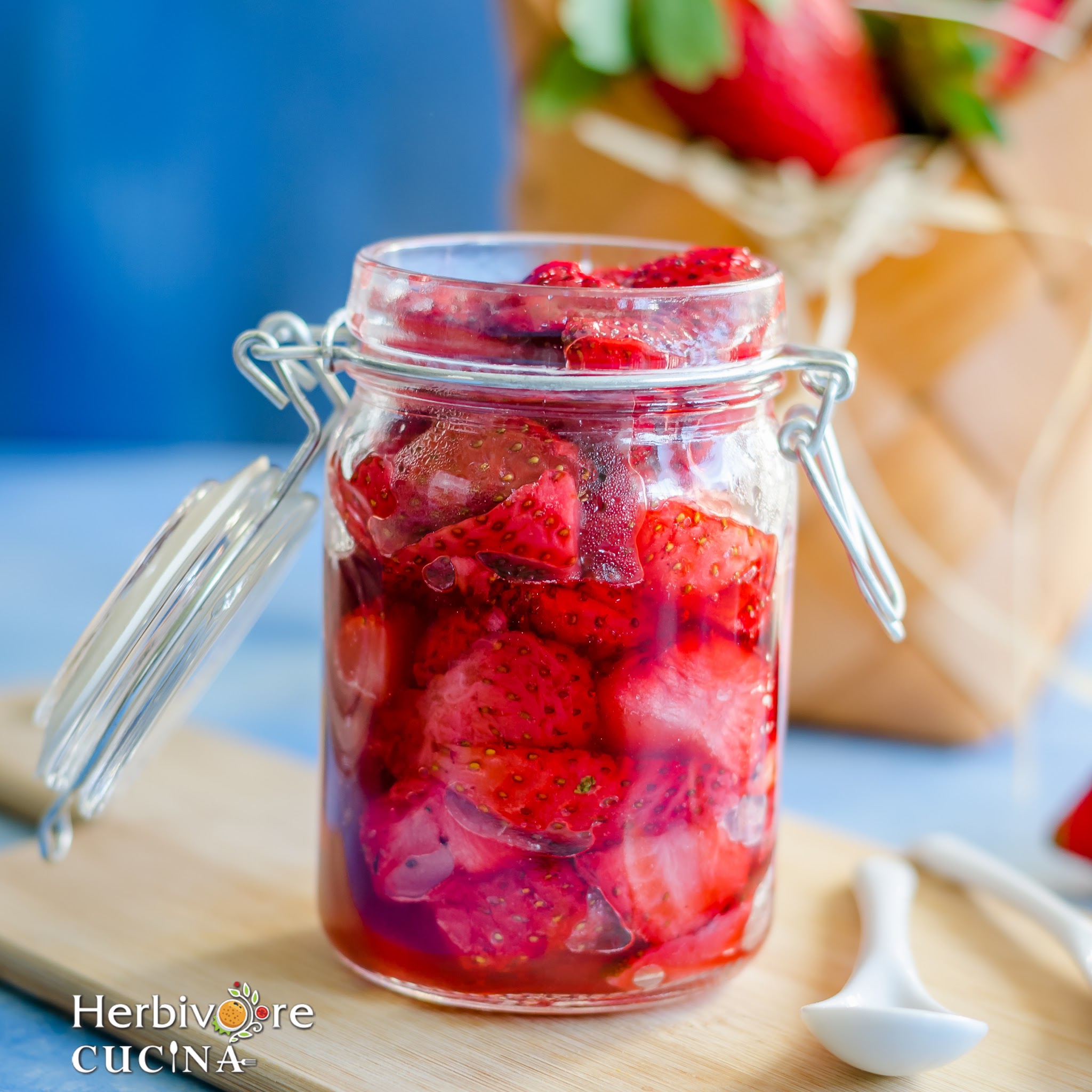 A glass jar filled with roasted strawberries and a spoon on the side with more berries behind it. 