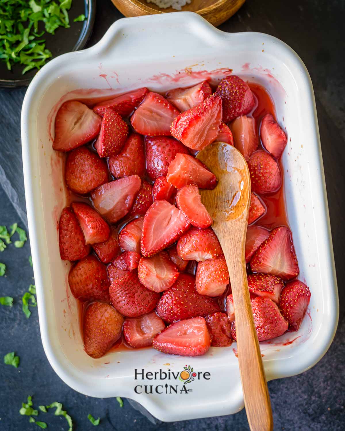 Roasted Strawberries in a white platter with a spoon on the side and leaves on the side. 