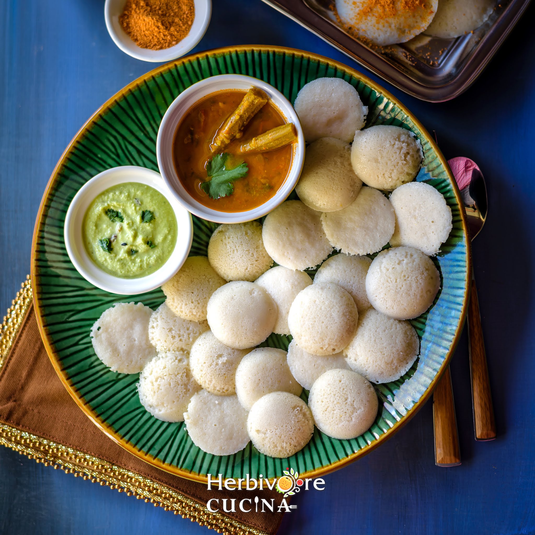 Instant Pot idli in a green plate with chutney and sambar around it in small bowls. 