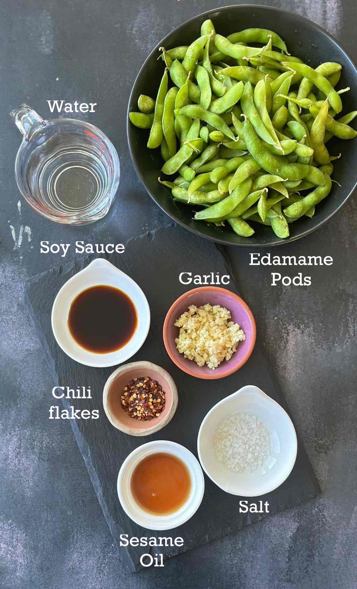 Ingredients for instant pot Garlic edamame in small bowls on a dark surface. 