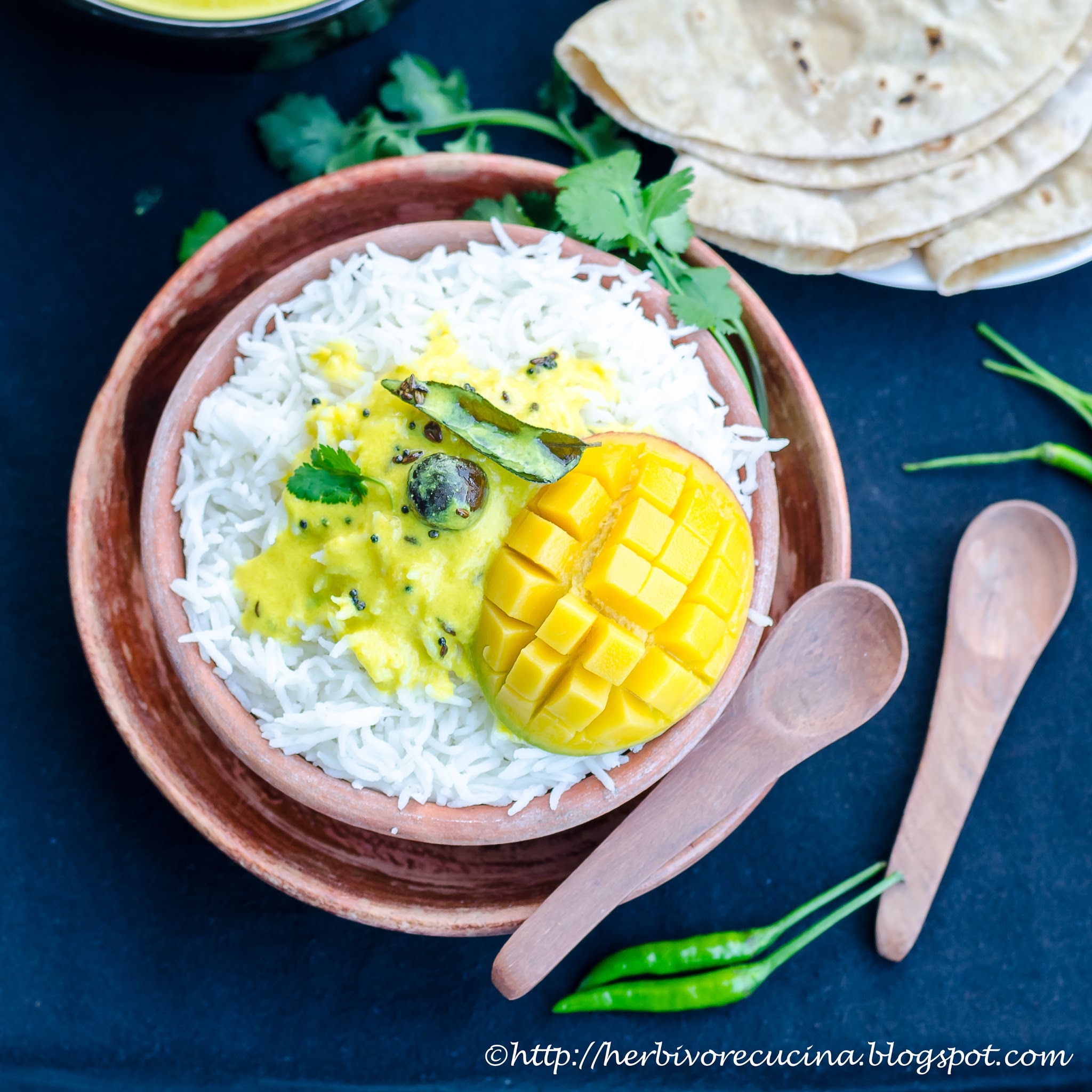 A bowl of steamed rice topped with fajeto and a slice of mango and served with some cilantro on top. 