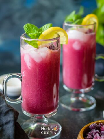 Two glasses filled with falsa sharbat and topped with mint leaves and lemon slices.