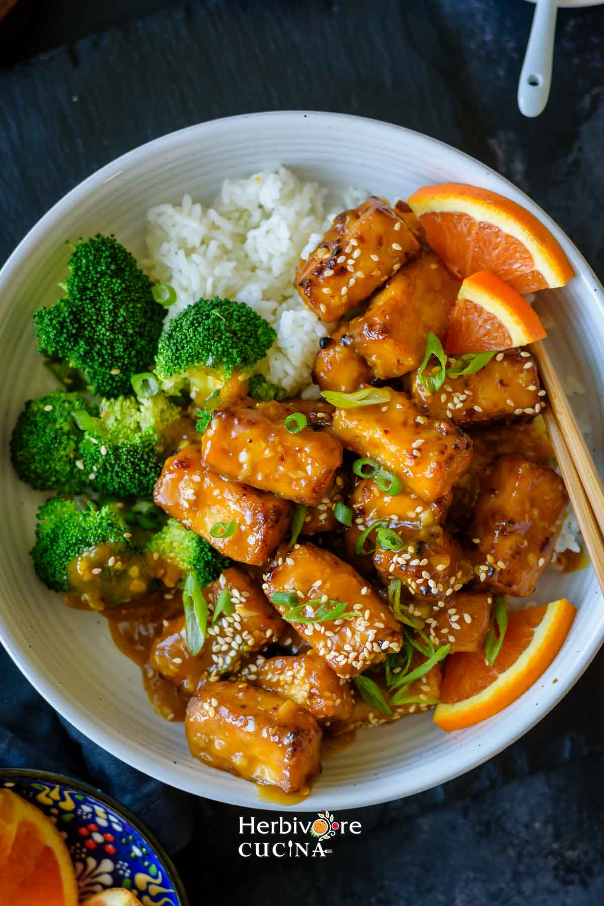 A white platter with orange tofu, some steamed broccoli and steamed rice. 