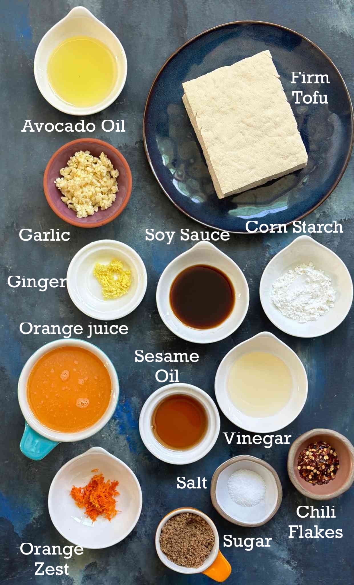 Ingredients for orange tofu arranged in small bowls on a dark surface. 