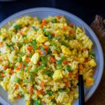 Jasmine fried rice in a gray plate with a fork on the side and topped with scallions, with a main dish on the side.