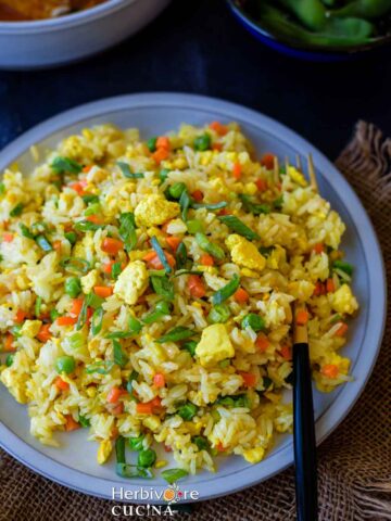 Jasmine fried rice in a gray plate with a fork on the side and topped with scallions, with a main dish on the side.