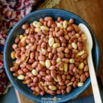 Air Fryer Peanuts in a blue bowl on a wooden board and a printed cloth on the side.