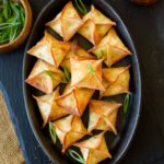 A black tray filled with cream cheese wontons with scallions and sauce on the side.