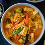 A white bowl filled with tofu panang curry with a spoon on the side.