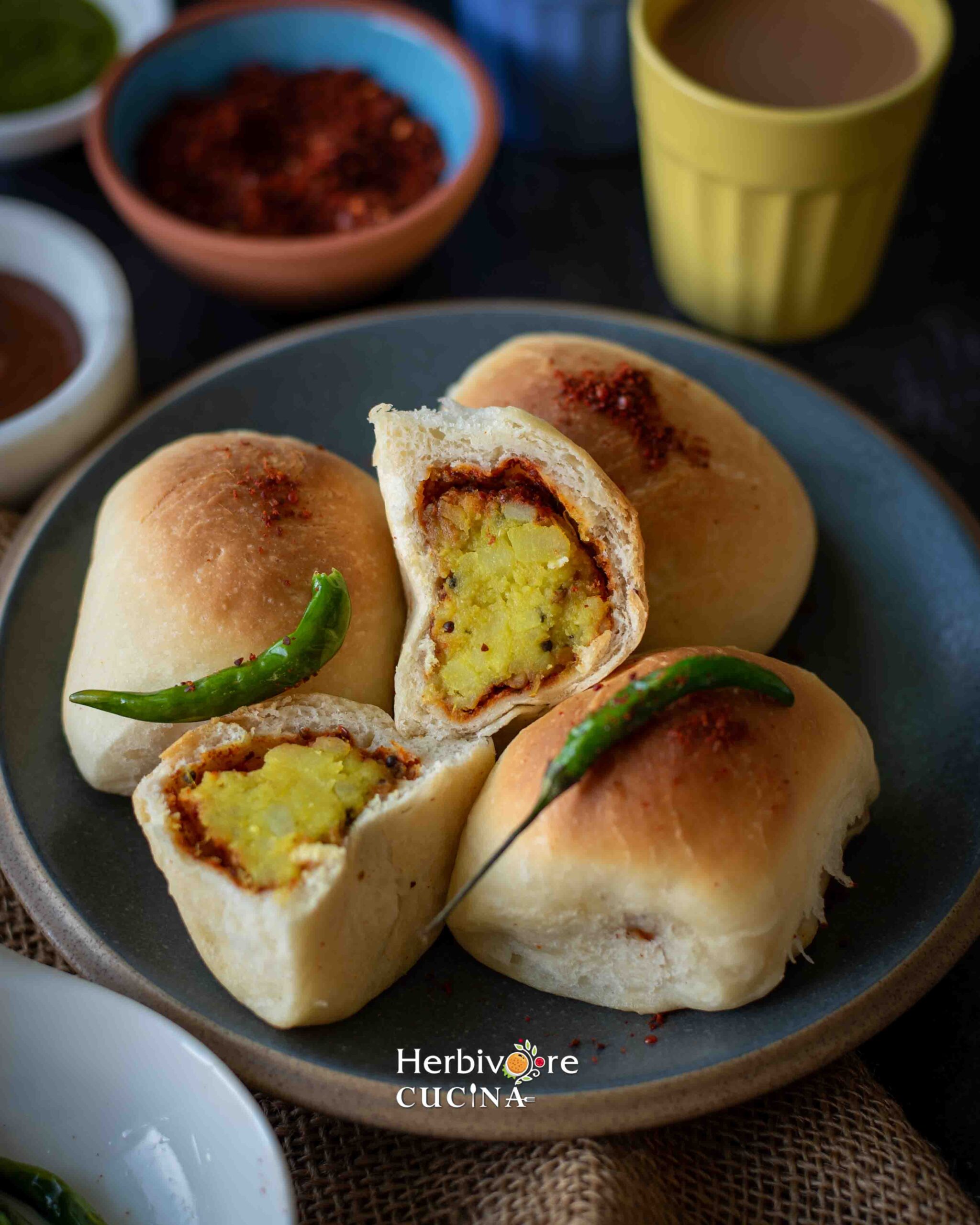 A plate with baked vada pav with one vada pav cut into half.
