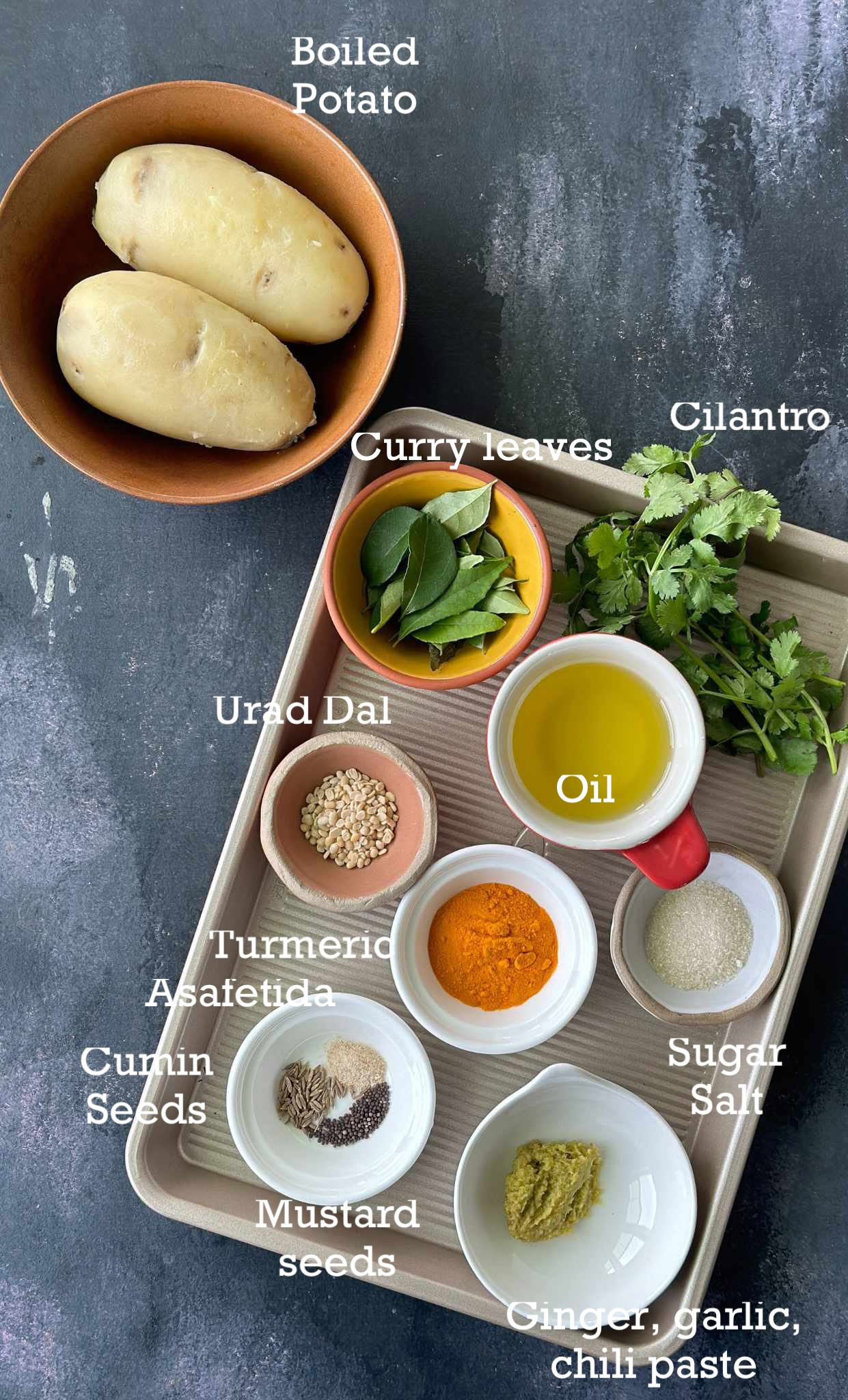 Ingredients for making baked vada in small bowls on a dark surface.